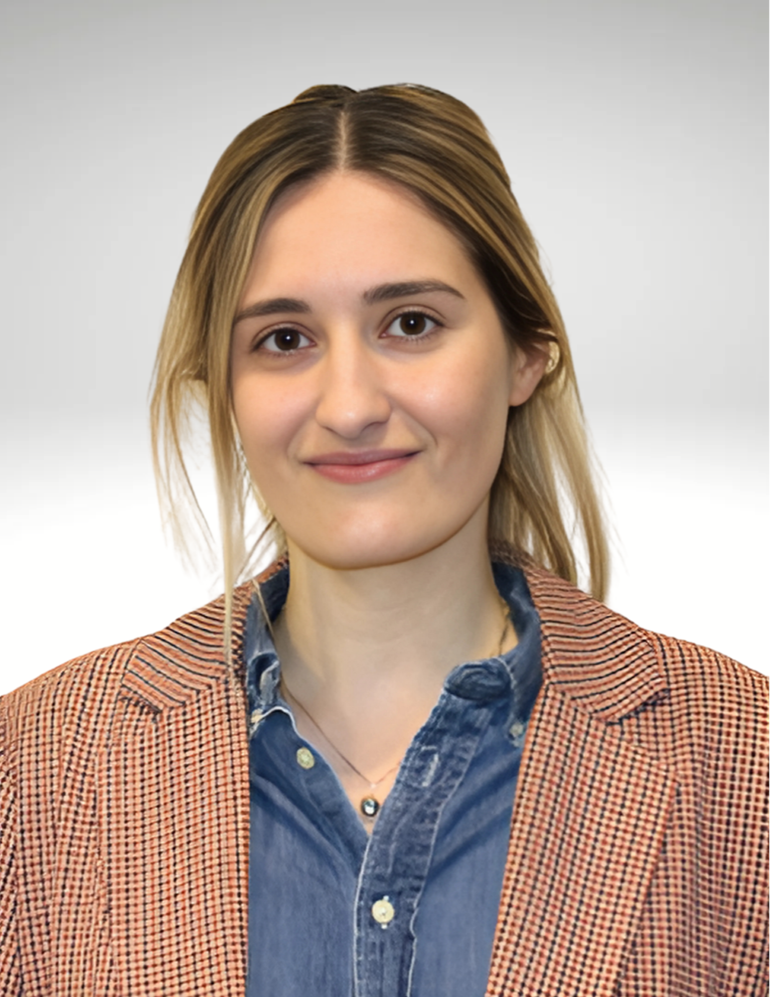 A woman with light hair smiles warmly, wearing a denim shirt under a brown plaid blazer. The background is a soft gradient, conveying a professional tone.