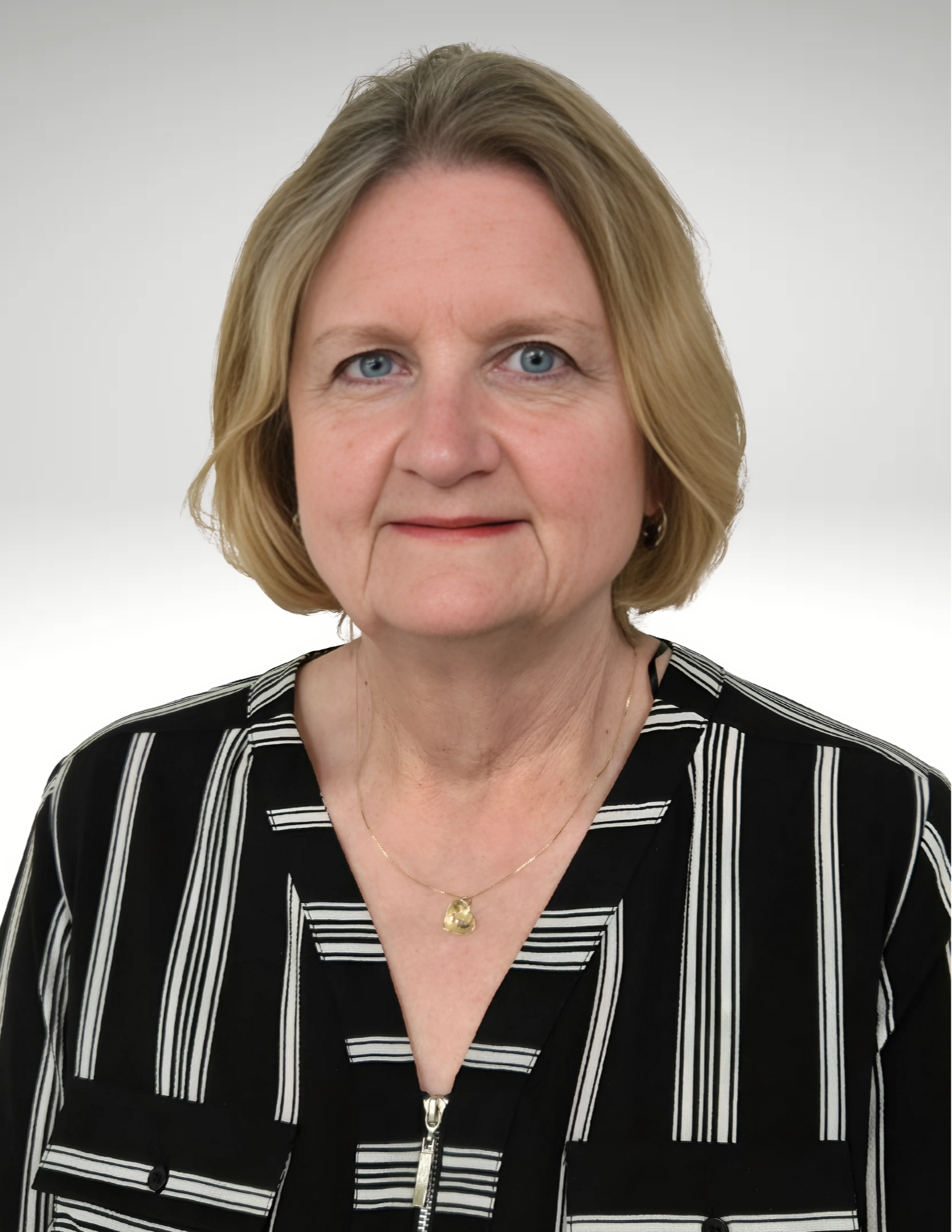 A woman with short, light hair wears a black and white striped blouse. She has a neutral expression and a pendant necklace, set against a plain background.