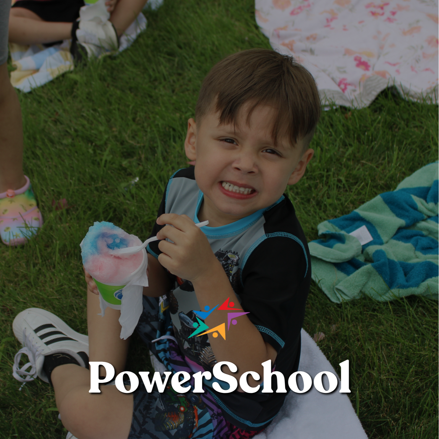 A smiling young boy sits on a white blanket in the grass, holding pink cotton candy at an outdoor gathering; the PowerSchool logo overlays the image.