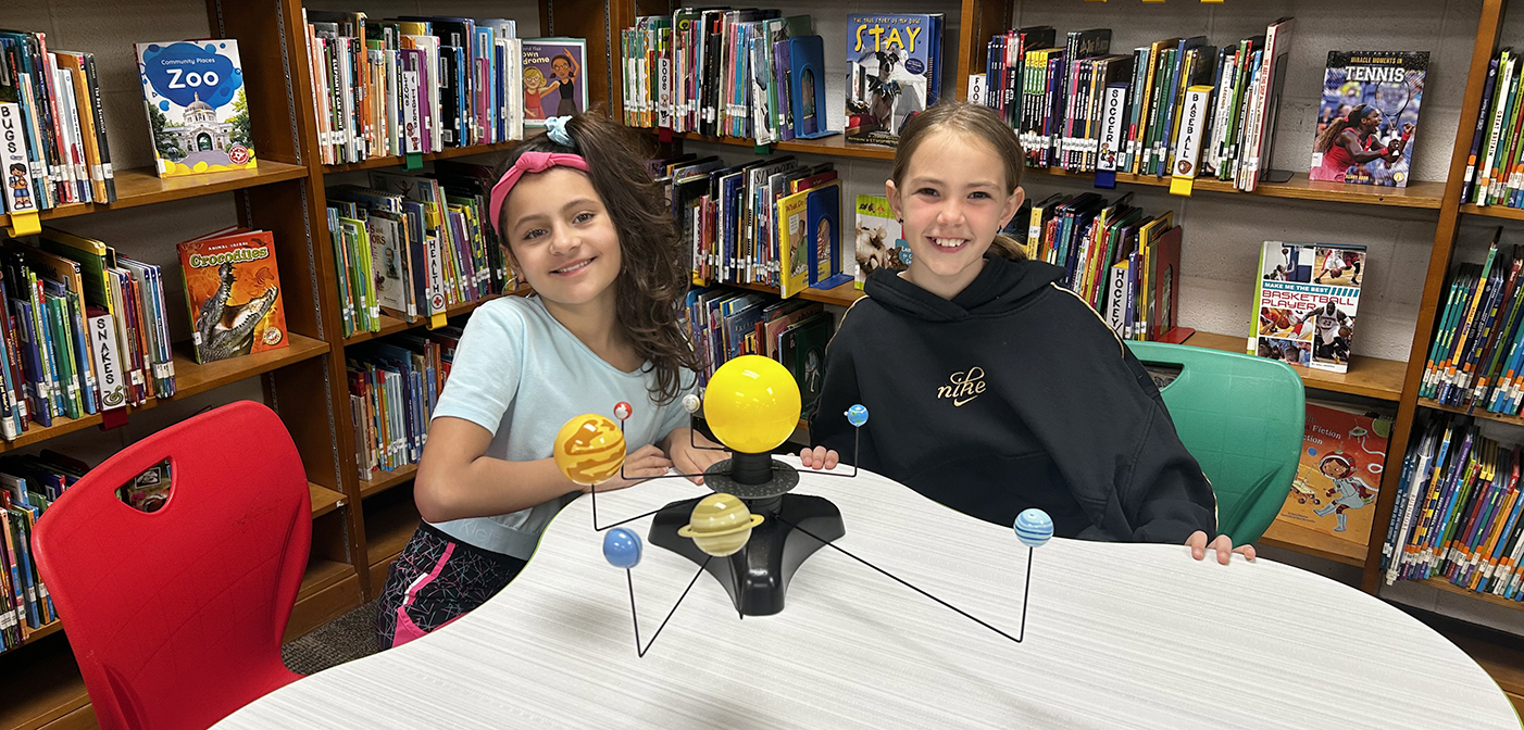 2 girls working with solar system model in the library