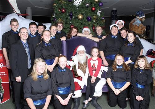 Miami East band posing with Santa Claus in front of  a Christmas tree.