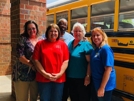 transportation staff smiling in front of a school bus