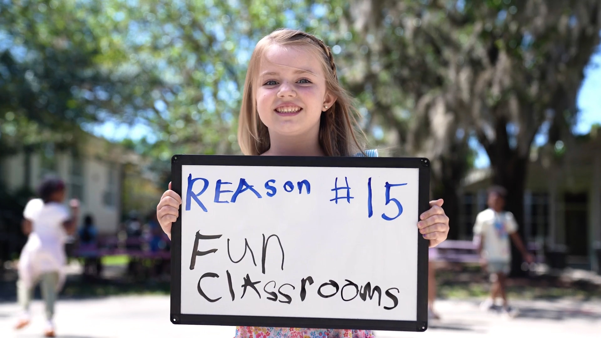 Girl holding a sign that states "Reason #15, Fun Classrooms"