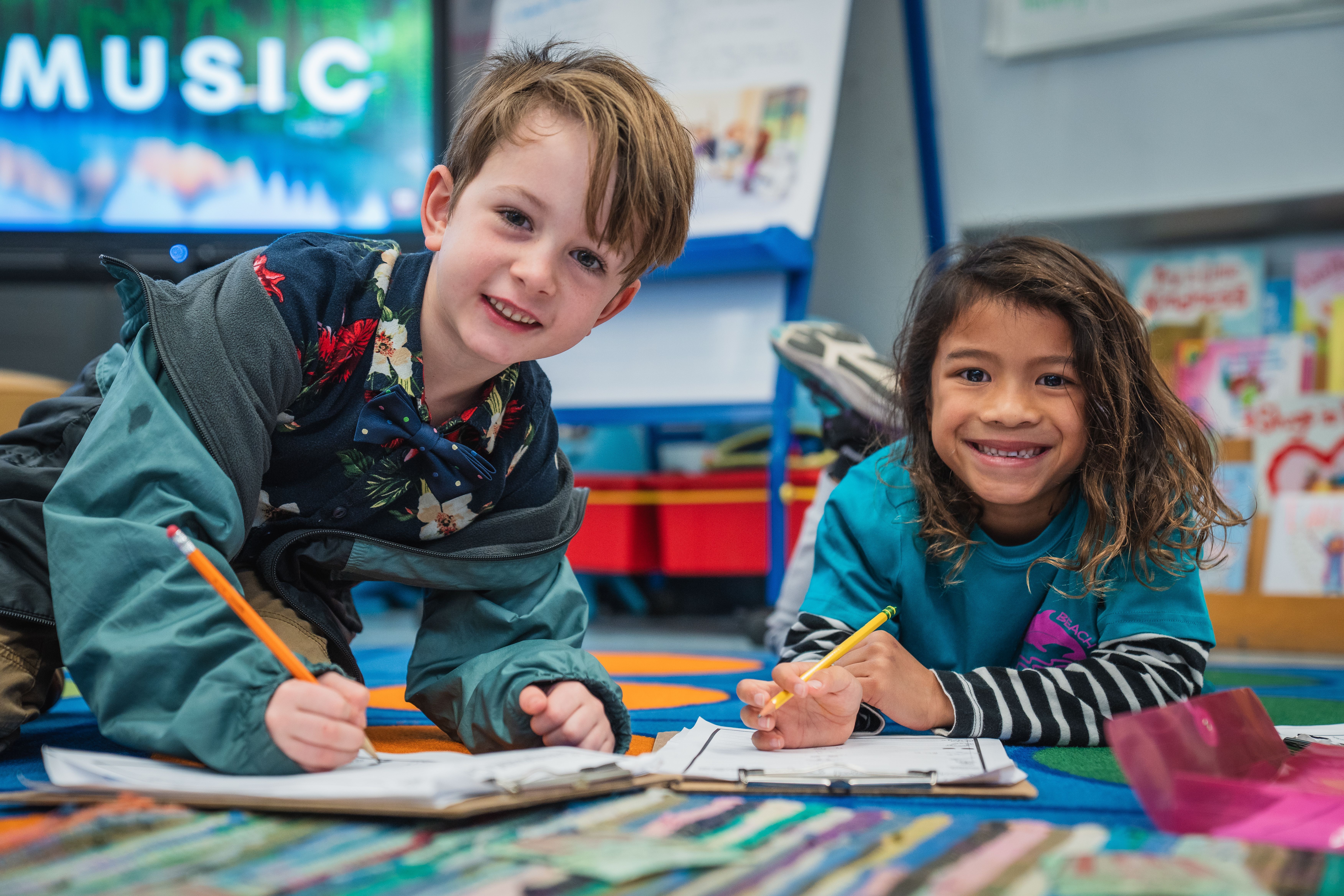 Two Duval County Public Schools elementary students on a carpet writing in notebooks and smiling