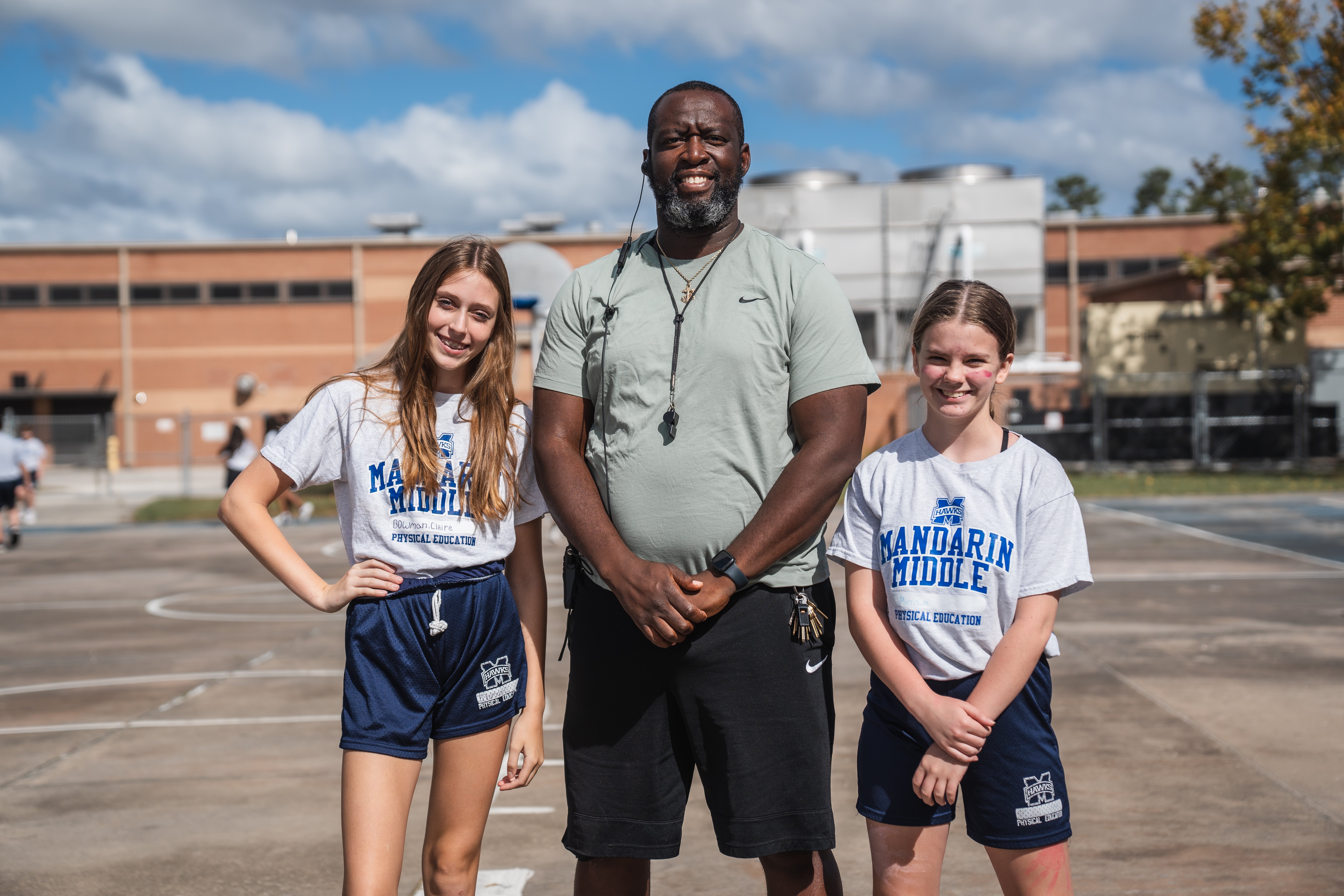 Mandarin Middle School PE Coach standing on court with a student on each side 