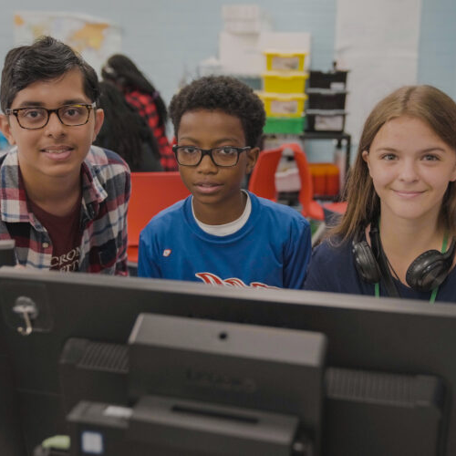 Three middle school students in front of a computer in class.