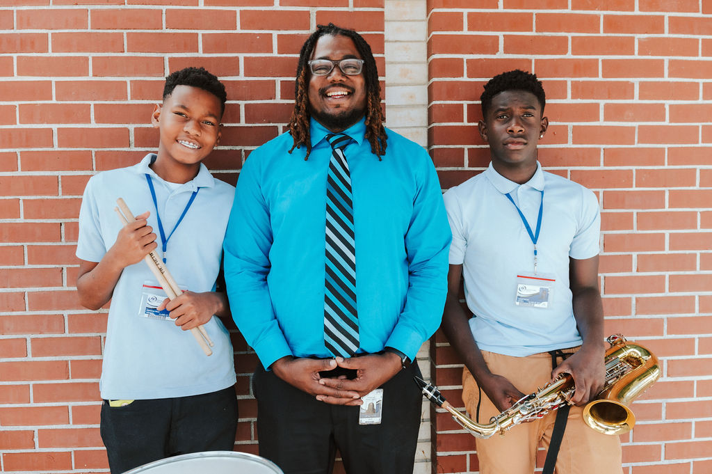 Music teacher posing with two middle school students holding instruments