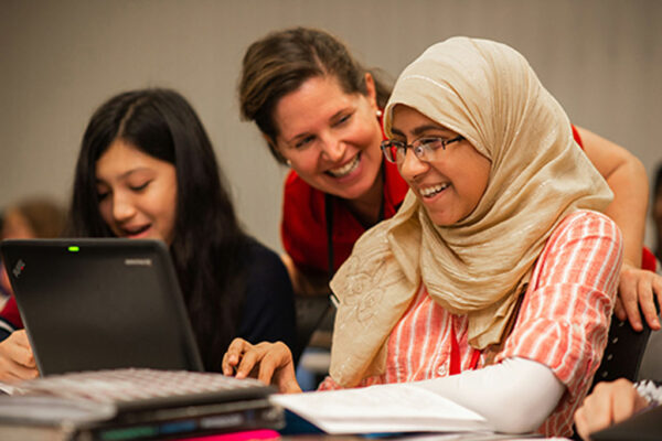 Students and teacher smiling while lookin at their laptops