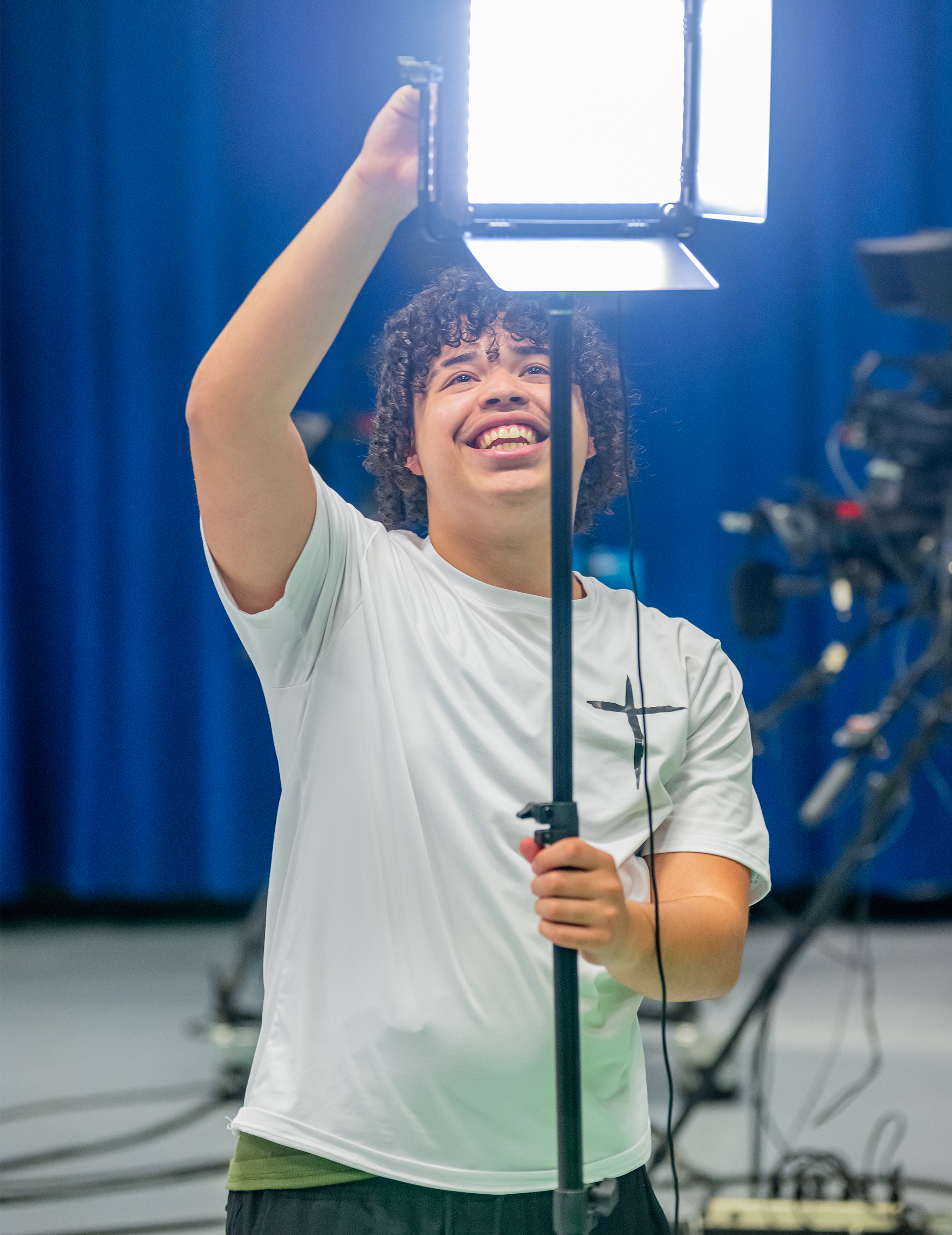 A young man positions a light over a camera, enhancing illumination for an upcoming photo shoot.