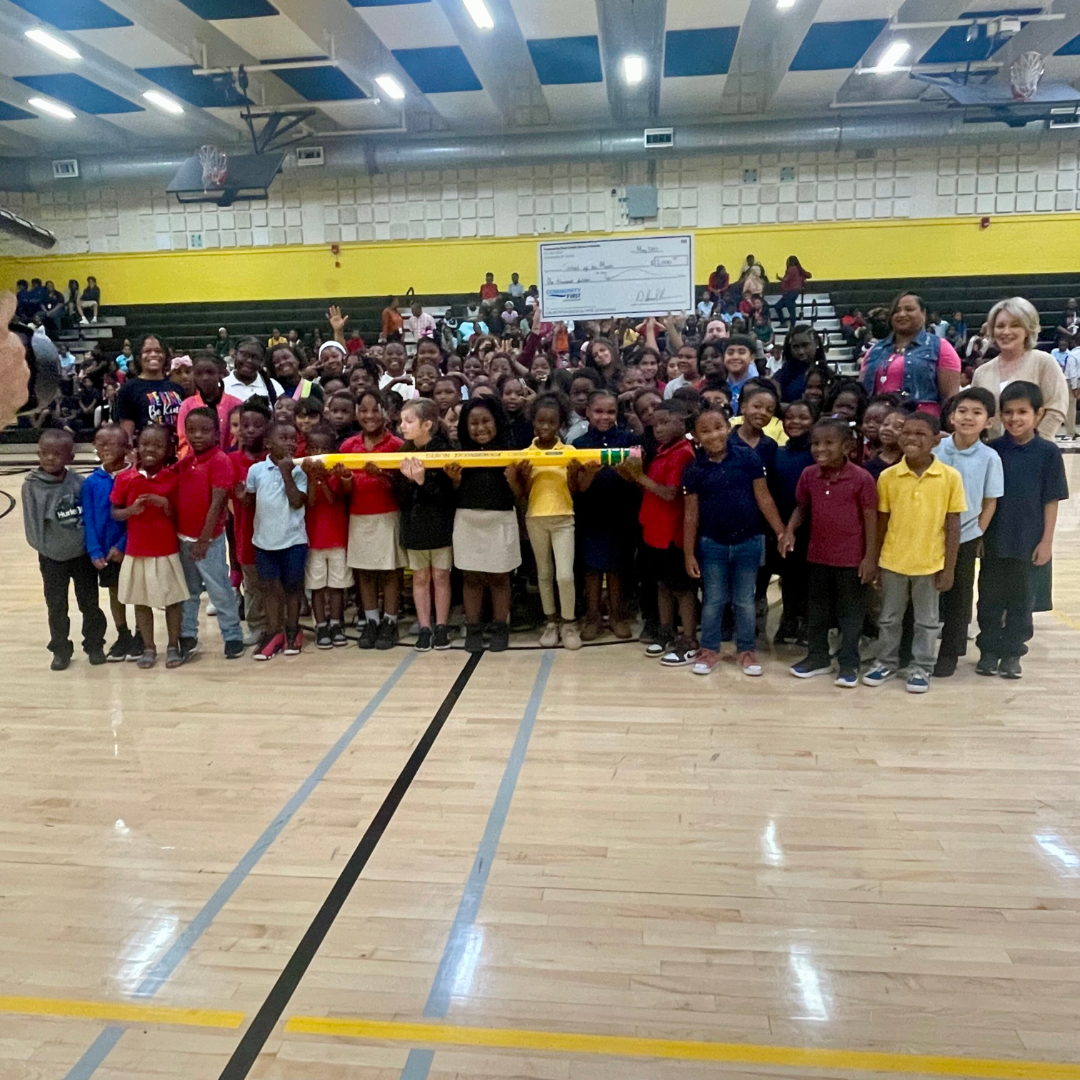 students, staff and partners smiling with large check and pencil