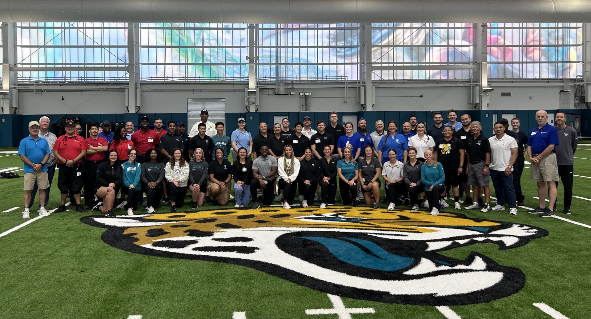A large group of men and women standing around the Jacksonville Jaguar's logo on the practice indoor field