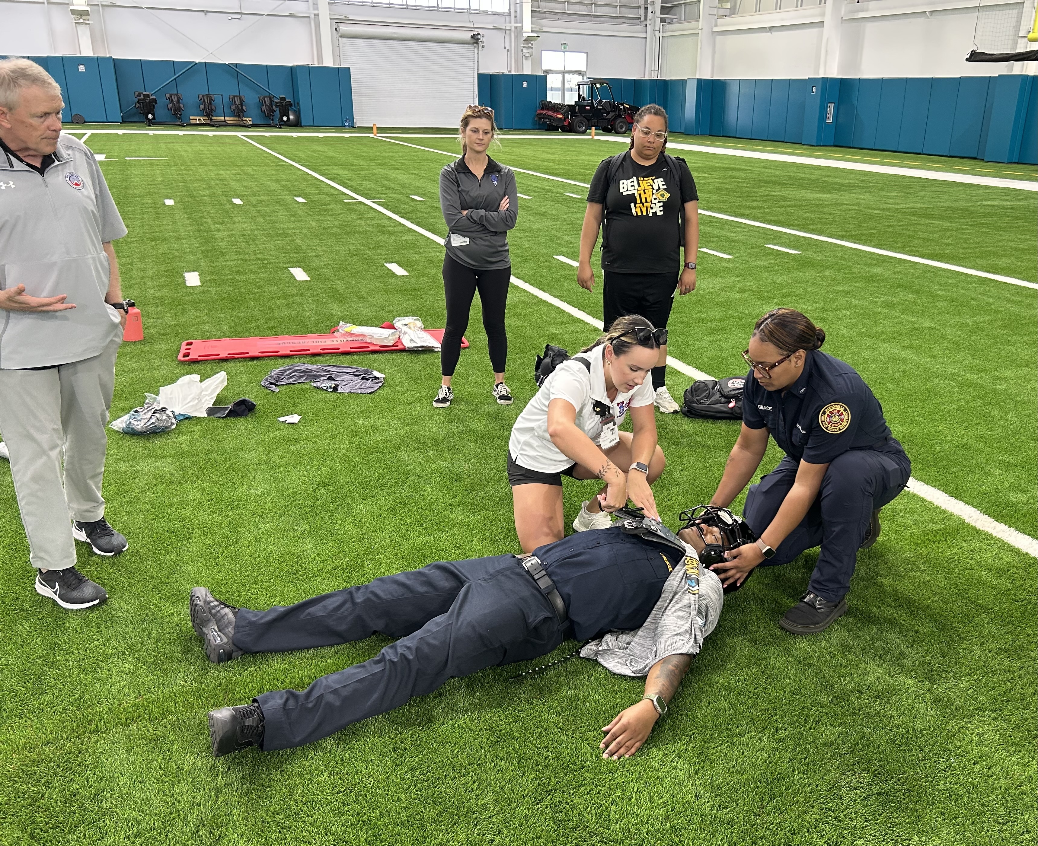 Two people practicing football equipment removal from a live model simulating an emergency scenario