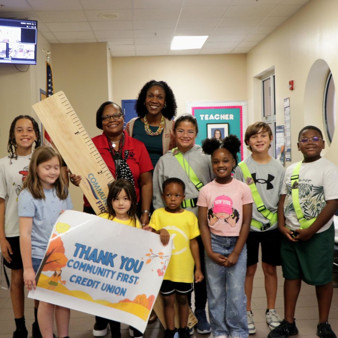 students smiling for a photo on stage with a large ruler and Thank You Community First Credit Union sign