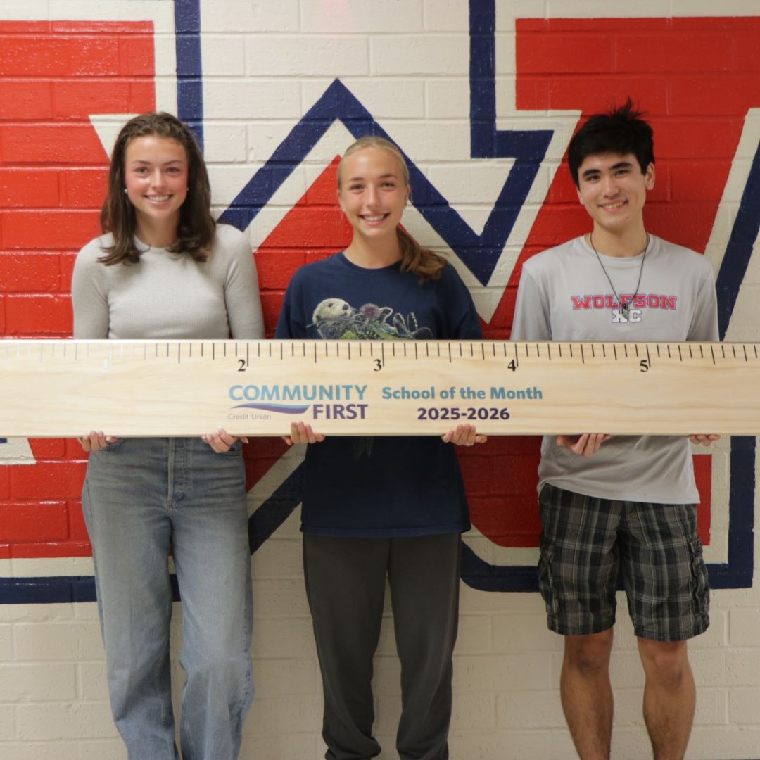 students smiling for a photo on stage with a large ruler