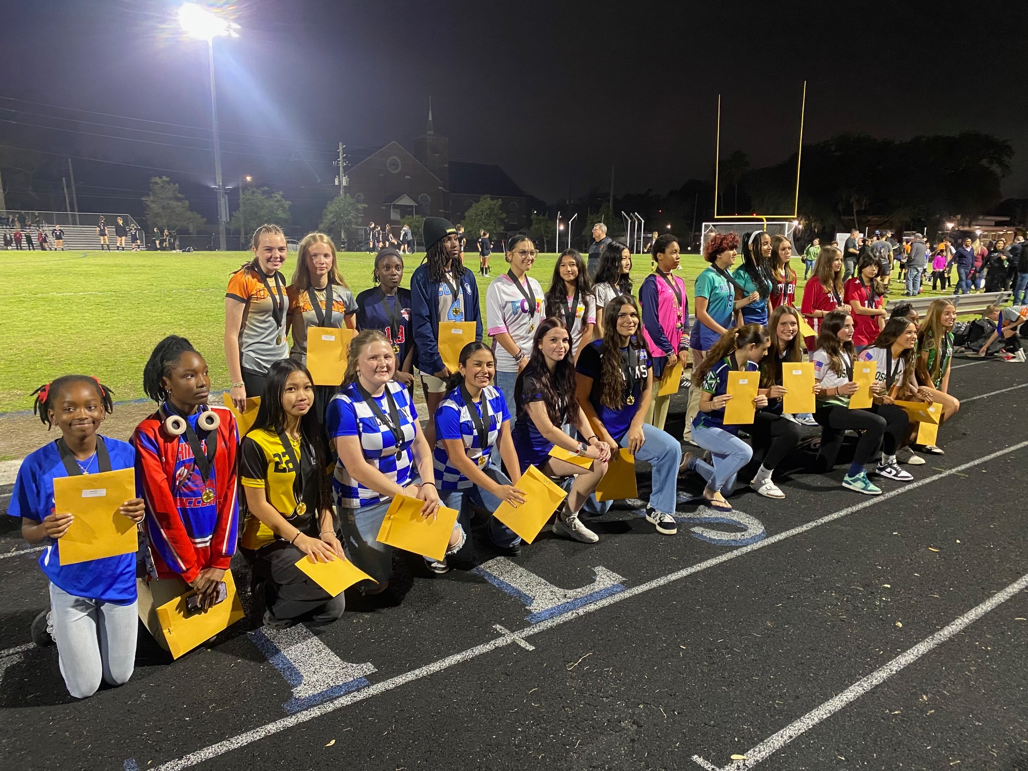 A group of individuals in athletic attire, holding certificates, poses for a photo on a track.
