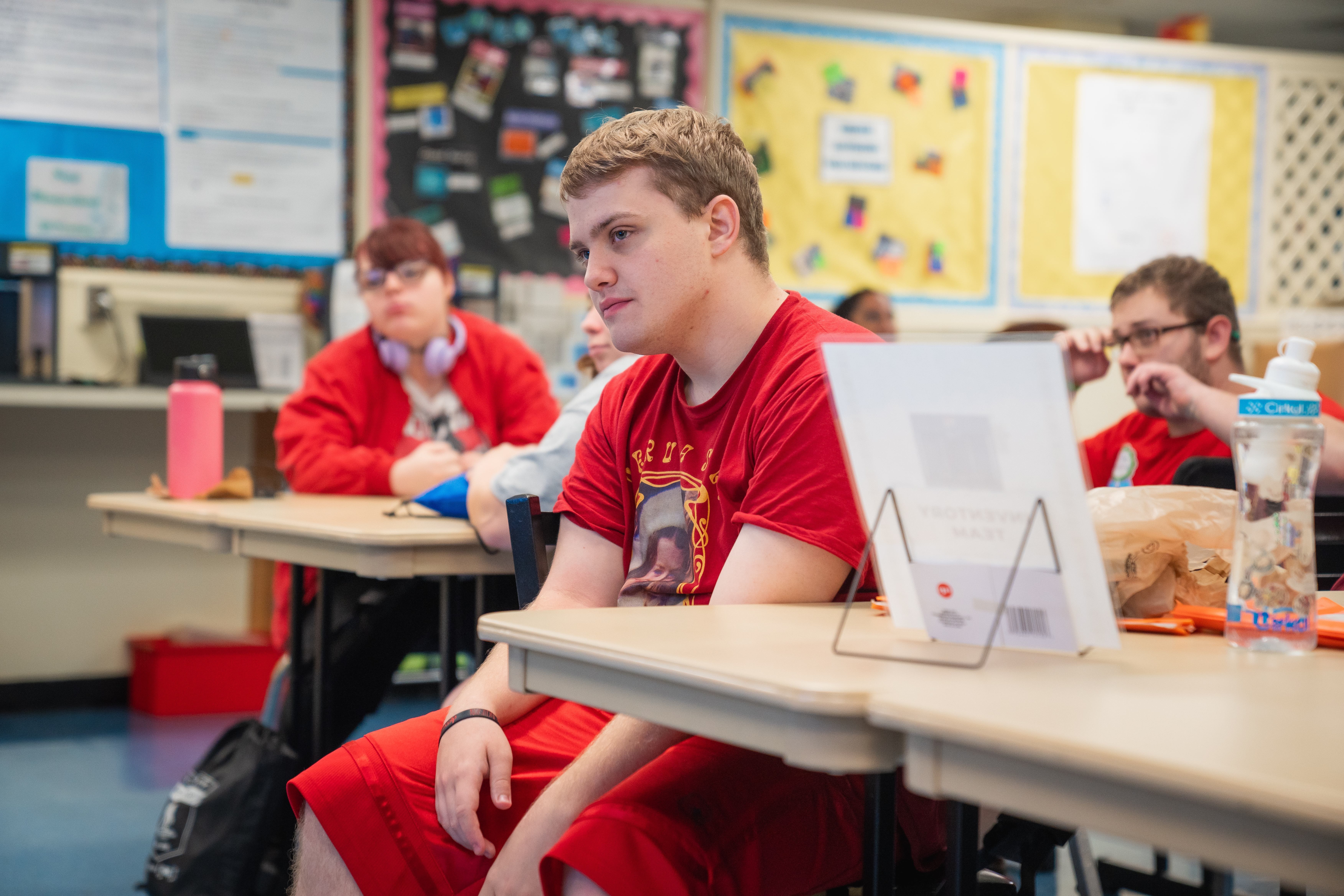 A classroom with students wearing red shirts. One student is looking away while sitting at a desk.