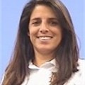 A woman with long, straight brown hair smiles, wearing a white collared shirt against a blue background.