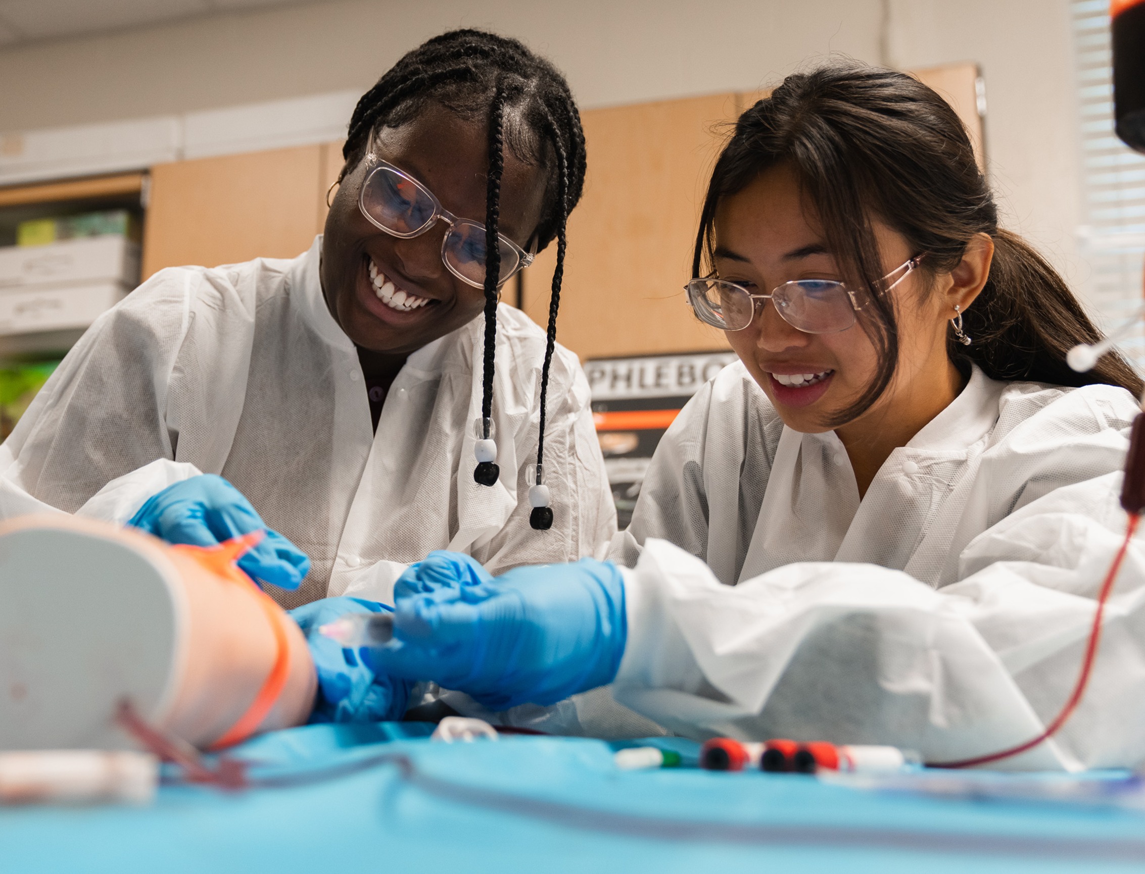 Two women in lab coats and glasses work on a project with a large orange and white object.