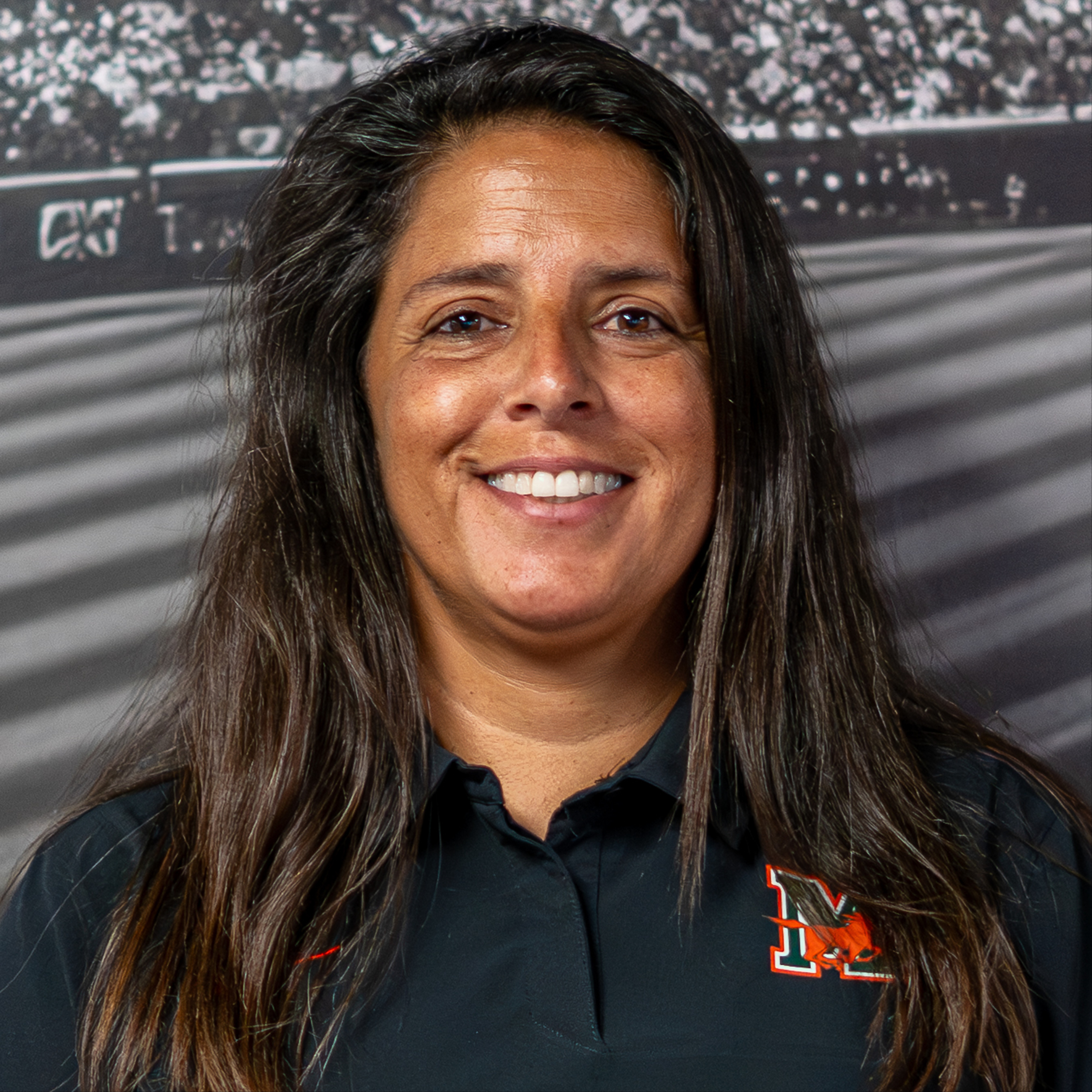 A smiling woman with long hair wearing a black shirt with a red logo on the left chest.