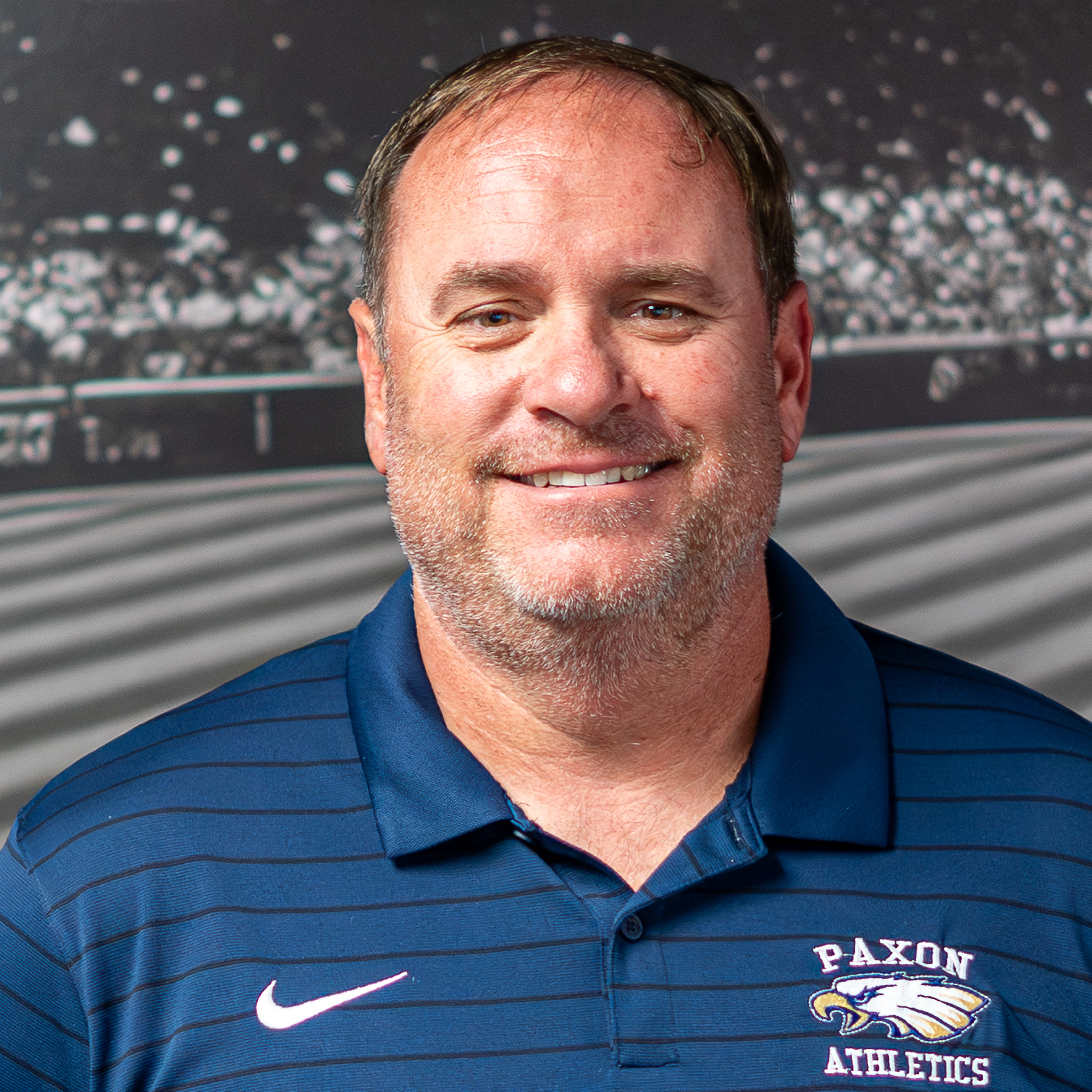 Man smiling, wearing a blue polo shirt with "PAXON ATHLETICS" and a Nike logo on the left chest.