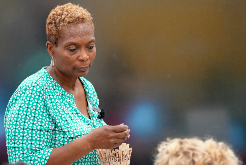 Woman with short hair and a green top holding a bundle of candles. Another person with blond hair appears behind.