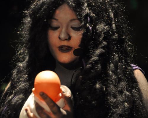 A woman with long black hair holding an orange, showcasing a vibrant contrast between her hair and the bright orange fruit.