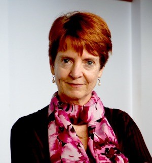 A woman with red hair and a pink scarf standing outdoors.