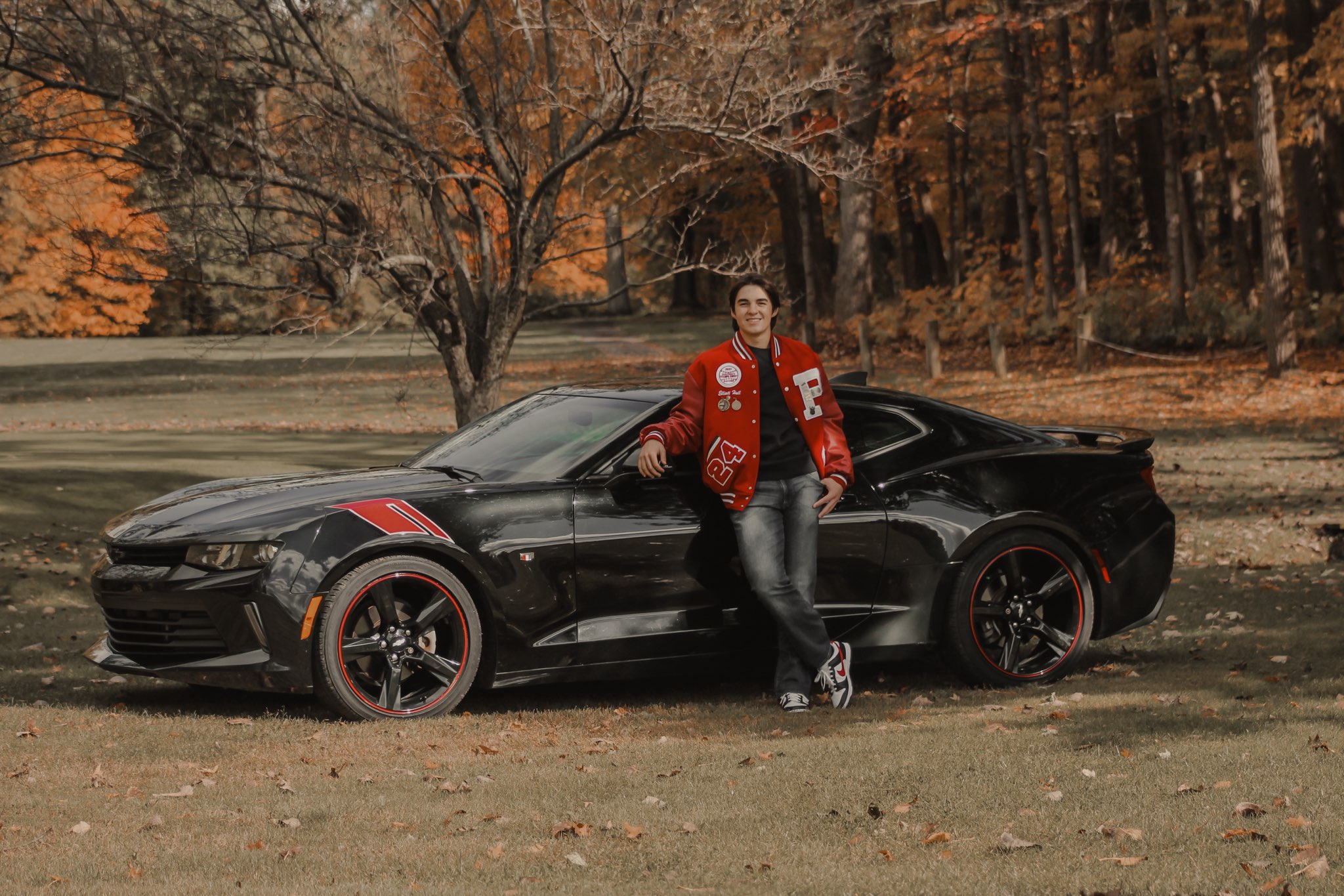 A man in a red jacket standing next to a black car.