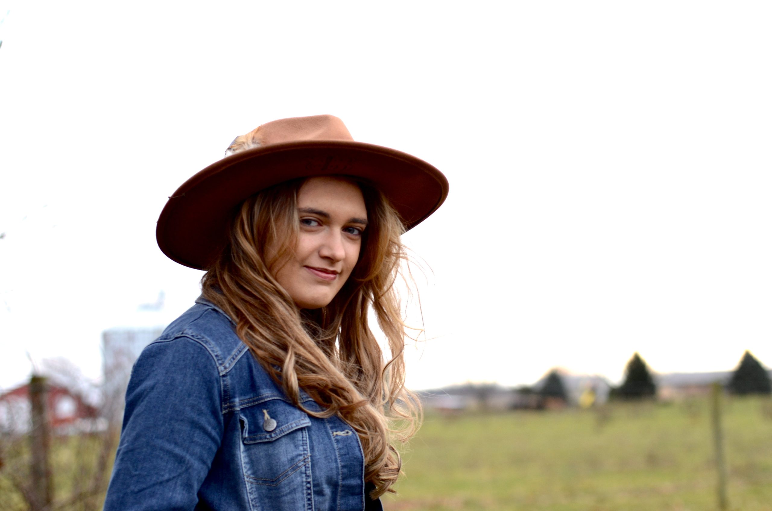 A woman in a hat and jeans standing in a field of wildflowers.