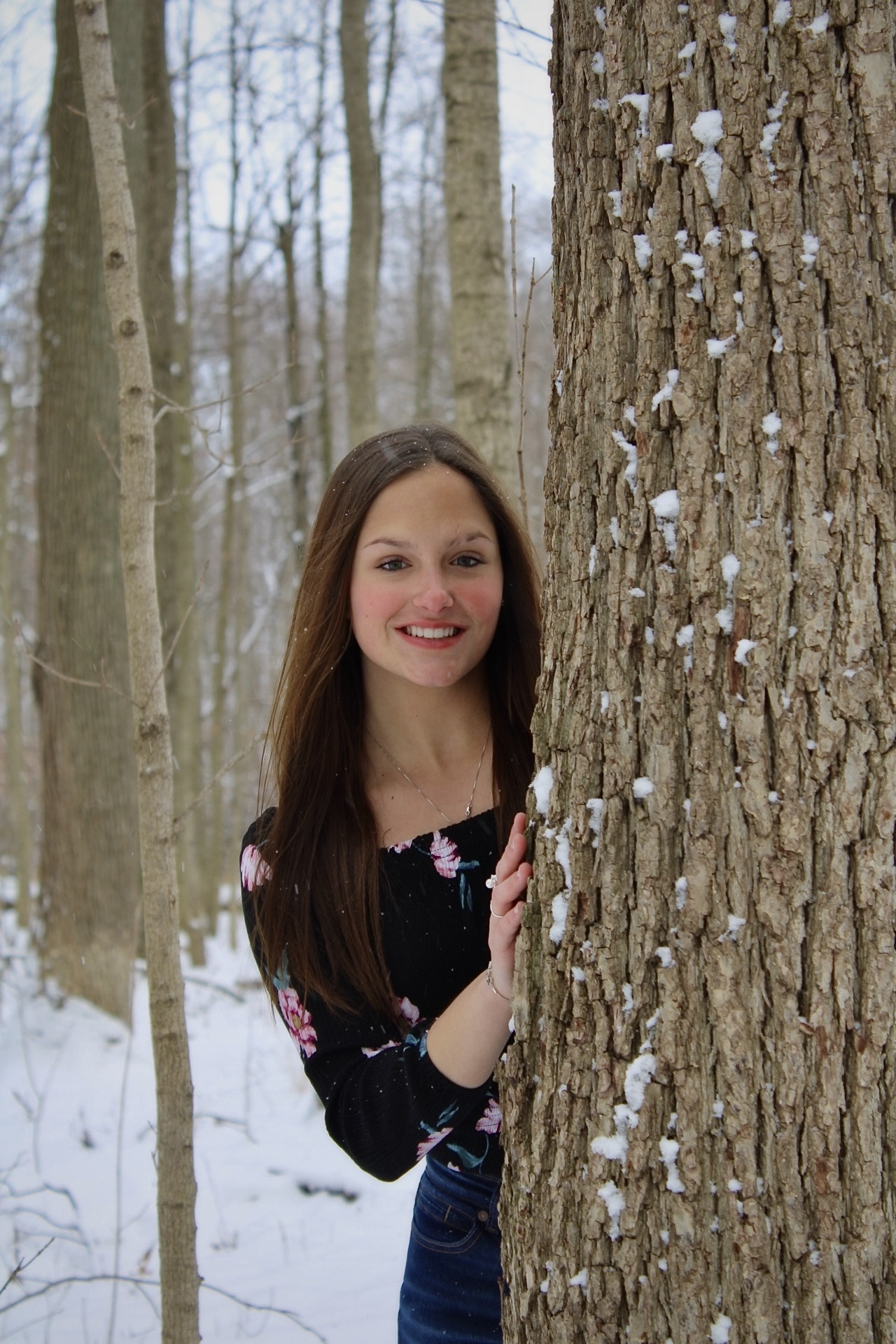 A girl leaning against a snow-covered tree, looking peaceful and serene in the winter landscape.