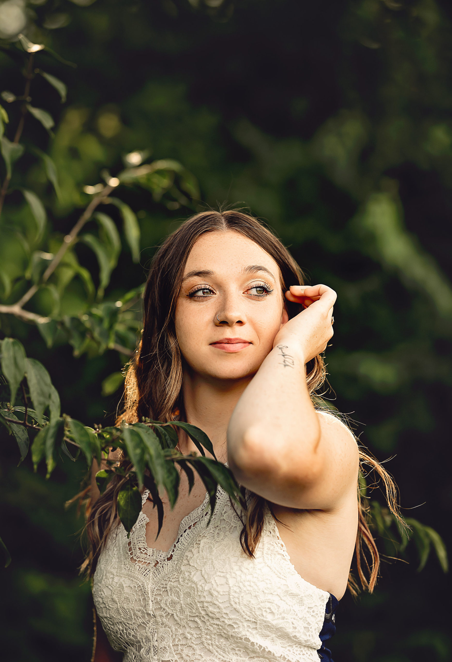 A stunning young woman in a white dress elegantly poses for a portrait, exuding grace and charm.