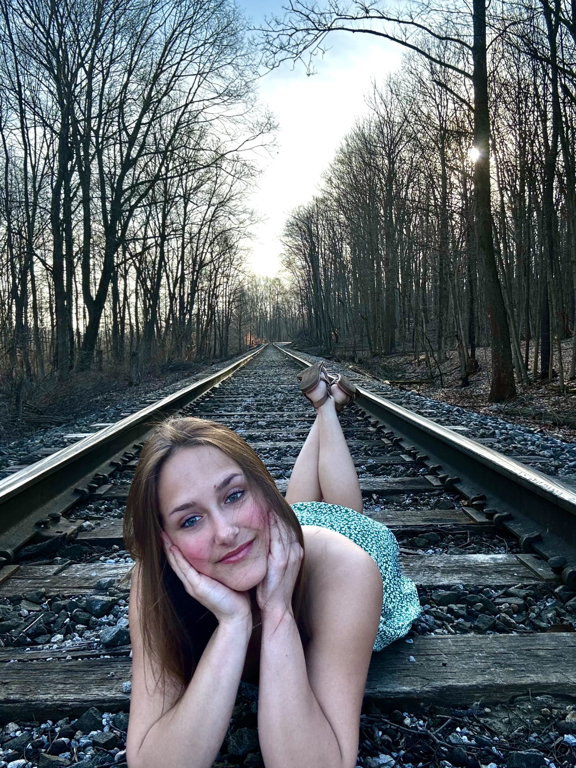 A young woman lies gracefully on the railroad tracks, exuding beauty and tranquility in her pose.