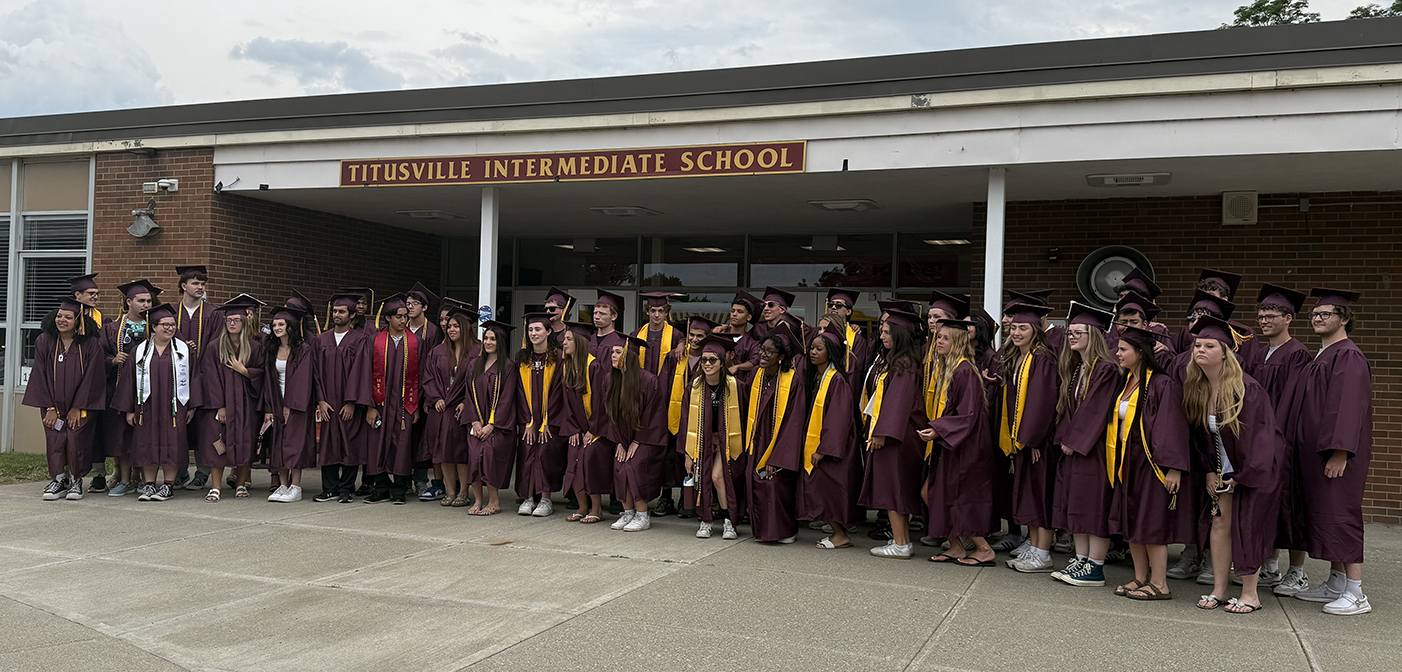 A group of AHS seniors in caps and gowns in front of Titusville school