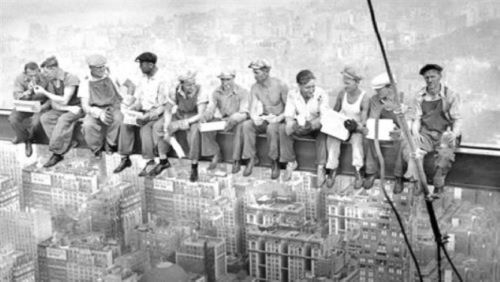 construction workers sitting on a piece of metal up in the sky