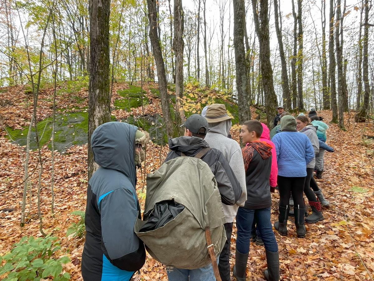 A diverse group of friends standing in the woods, surrounded by tall trees and sunlight filtering through the leaves.