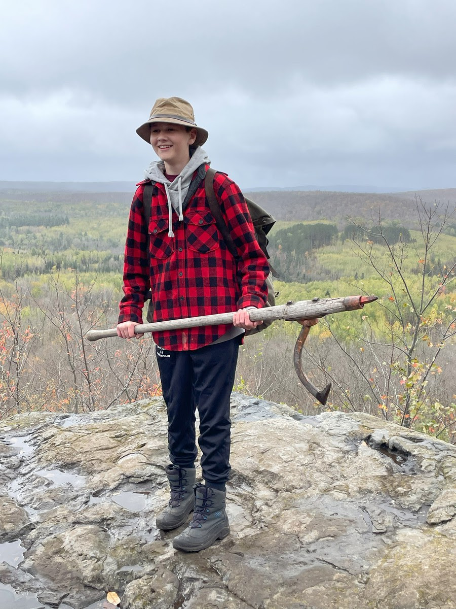 A woman in a plaid shirt and hat confidently holds a pickaxe, ready for some serious digging.