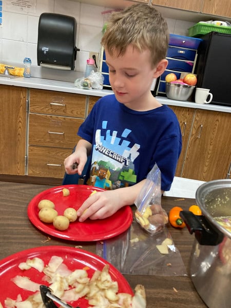 A young boy skillfully cutting potatoes on a plate with a knife.