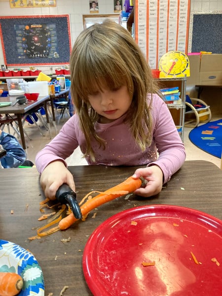 Child chopping carrots on a table.