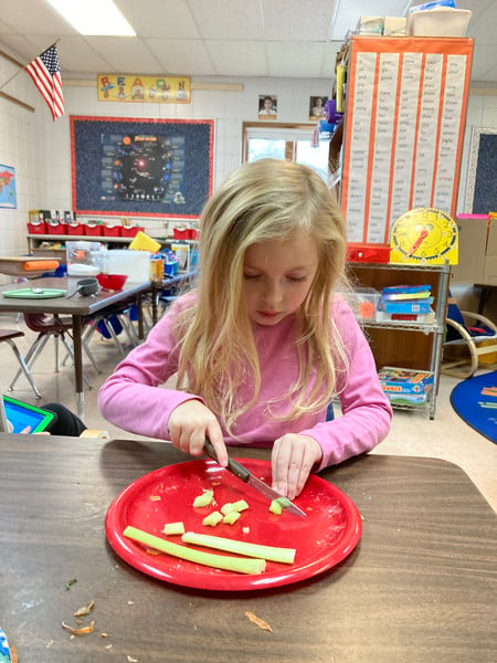 Child chopping potato on a table.