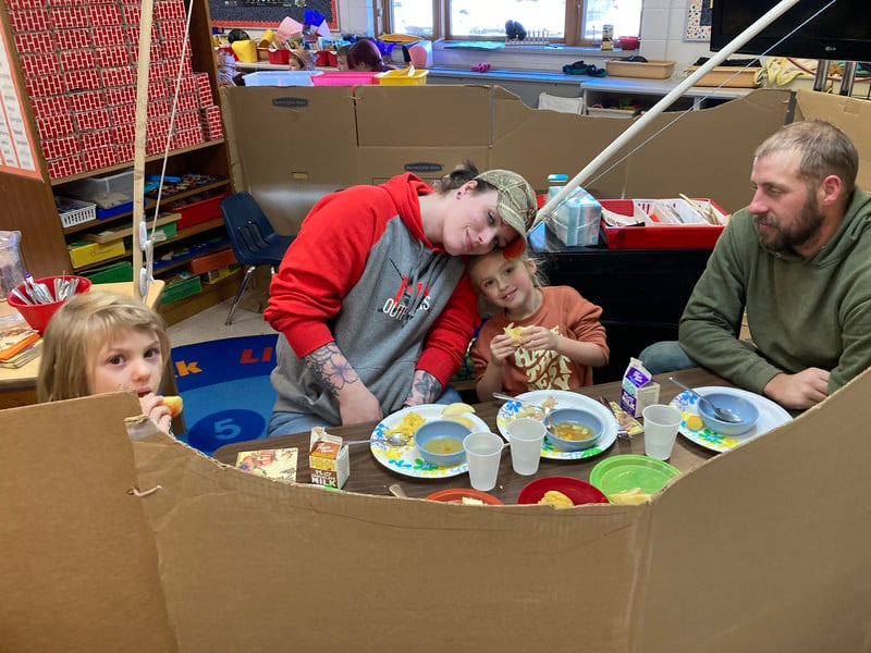 A family happily eating food while sitting inside a cardboard box.