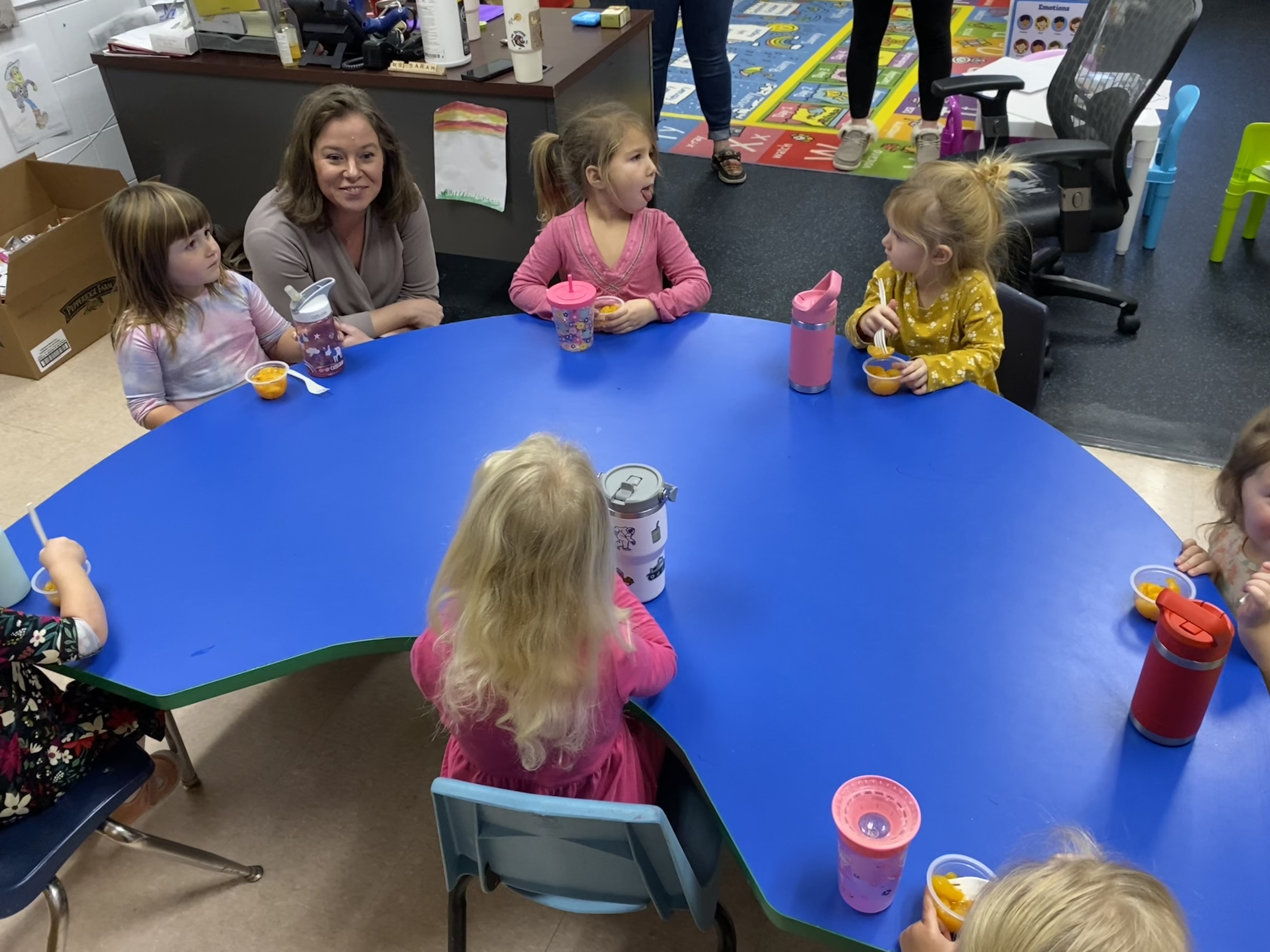 Group of kids gathered around a blue table, engaged in activities.