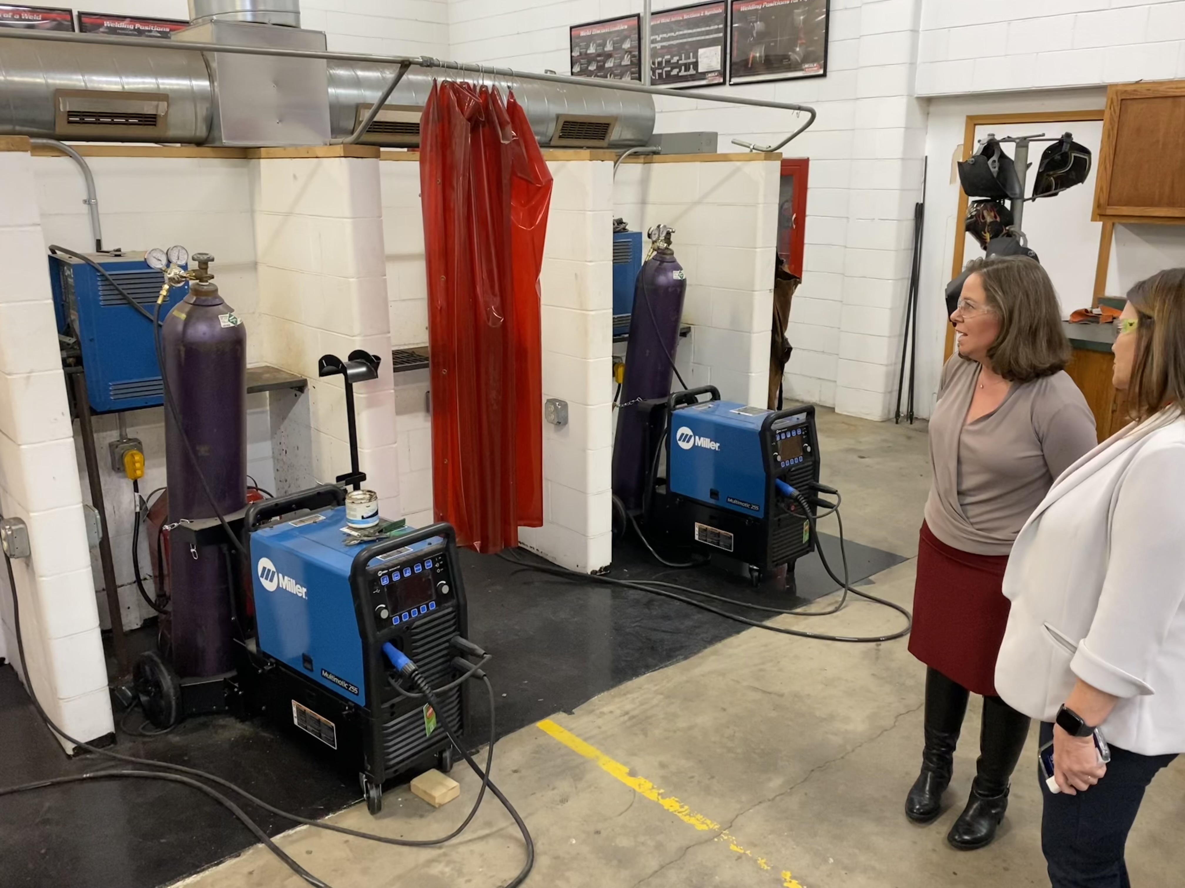 Image of two women in front of a welding machine, both wearing safety equipment.