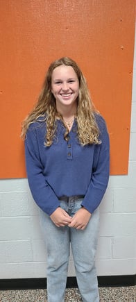 A girl in jeans and a blue shirt standing in front of an orange wall.