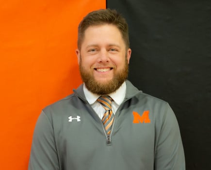 A smiling man with a beard wearing a grey shirt.