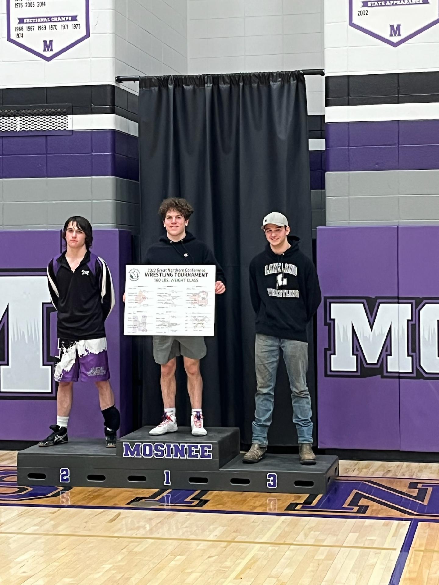 Three boys smiling on a podium holding a check.