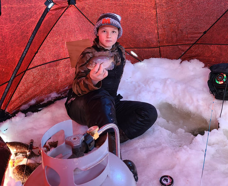 A young boy sitting in the snow, holding a fish.