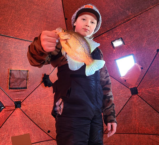 A young boy proudly holds up a fish inside a tent, showcasing his fishing success in the great outdoors.