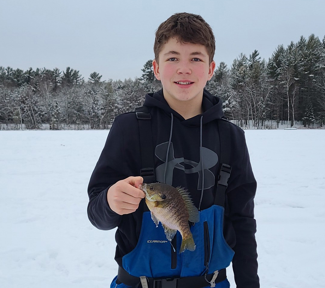 A boy holding a small fish in the snow.