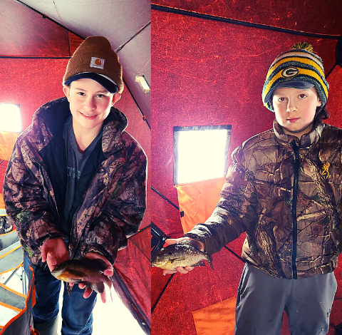 Two boys standing in a tent, holding fish they caught while camping.