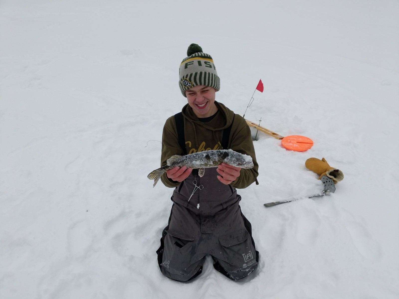 A man kneeling in the snow, holding a fish.